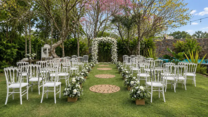 Ceremonia de día en el jardín: sillas blancas, un camino de alfombras de yute y un arco de flores blancas bajo lapachos en flor