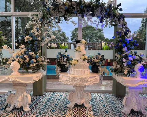 Mesa de graduación con arco de flores azules y blancas, frente a la piscina