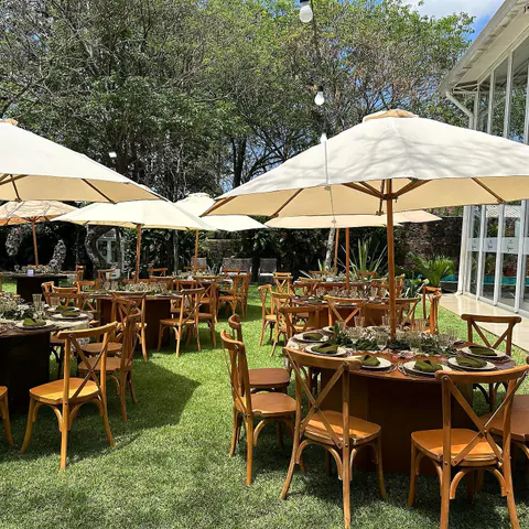 Mesas de madera y sombrillas en el jardín para una recepción de día