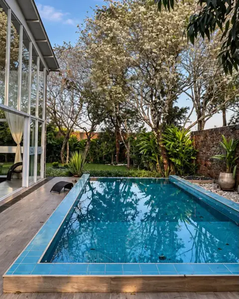 La piscina de venecitas junto al salón vidriado, con árboles en flor