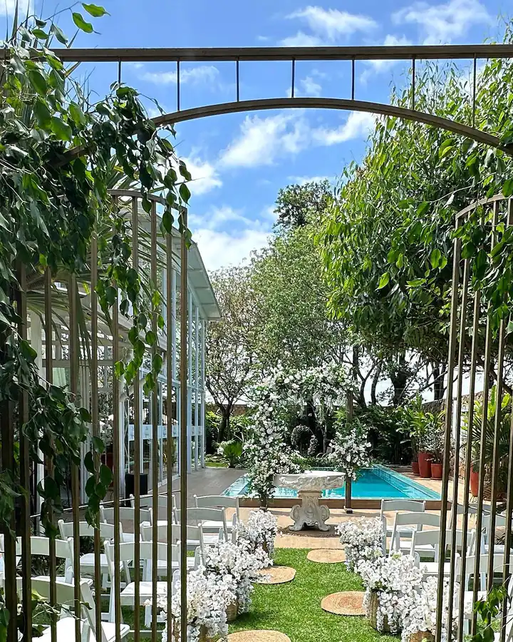El portón de hierro con enredaderas, abierto hacia el jardín y el salón vidriado, de día