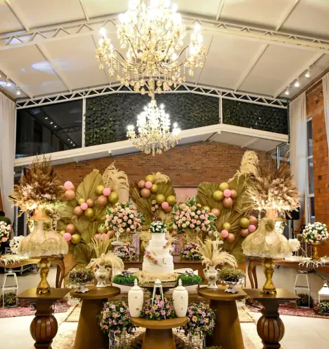 Mesa dulce boho chic con globos rosados y dorados, bajo dos arañas de cristal