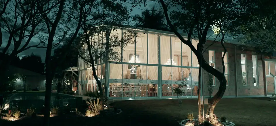 El salón vidriado iluminado de noche, entre los árboles del jardín